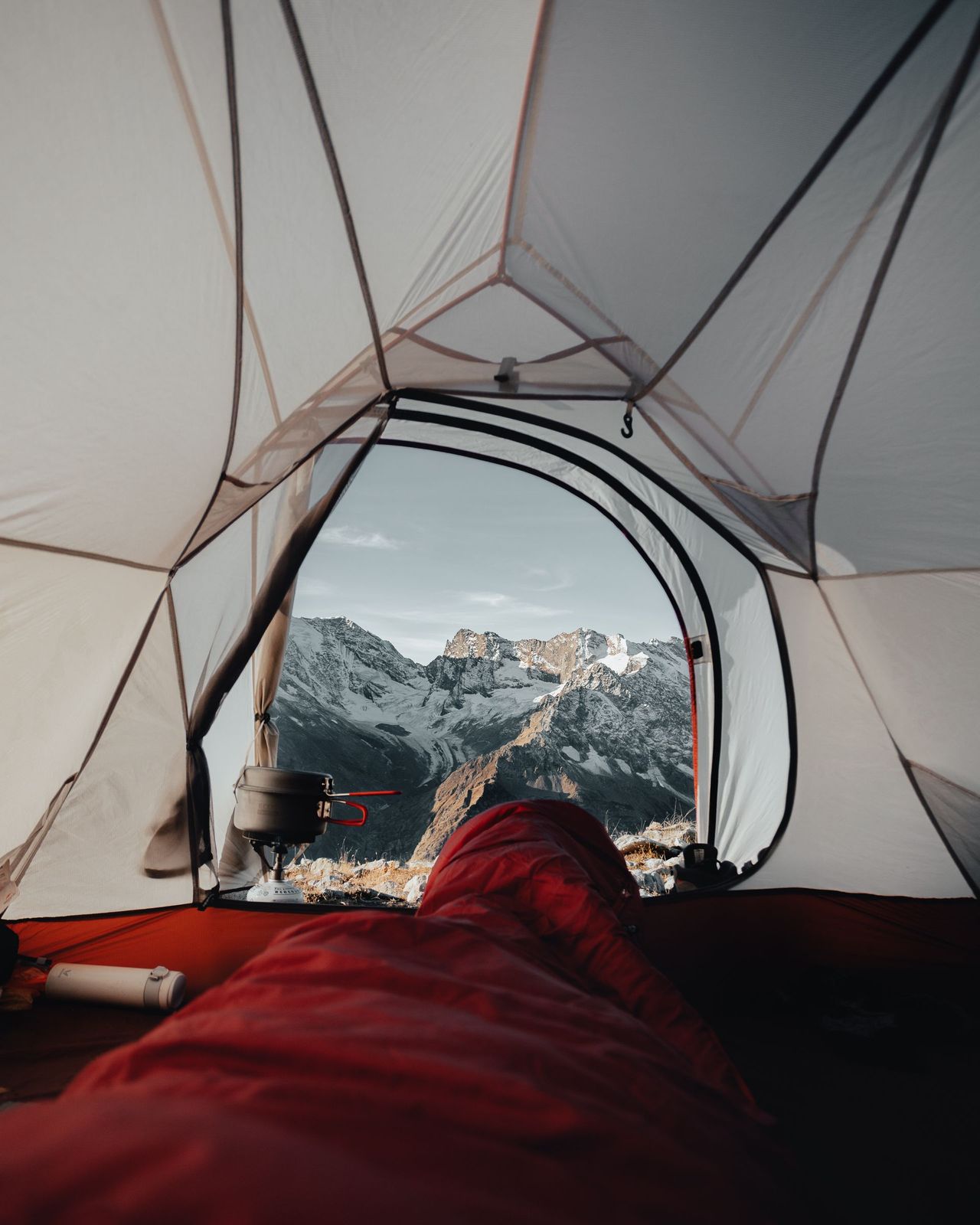 View from inside a tent over a red expedition sleeping bag toward snowy mountain peaks