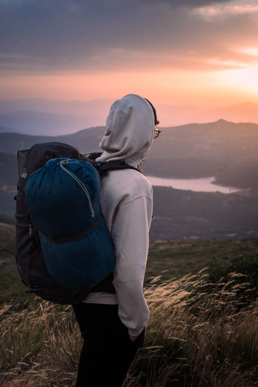 Backpacker overlooking a mountain lake with a compressed sleeping bag on the pack