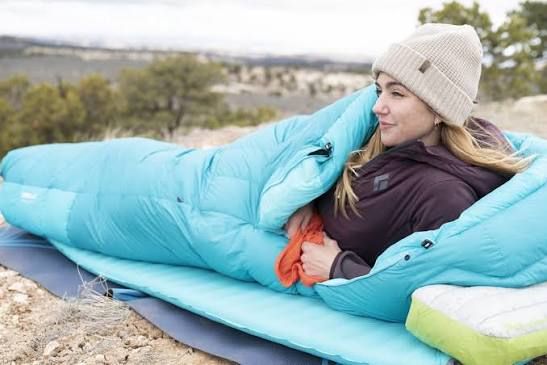Woman resting outdoors inside a teal Glacier Loft down mummy sleeping bag on an insulated pad
